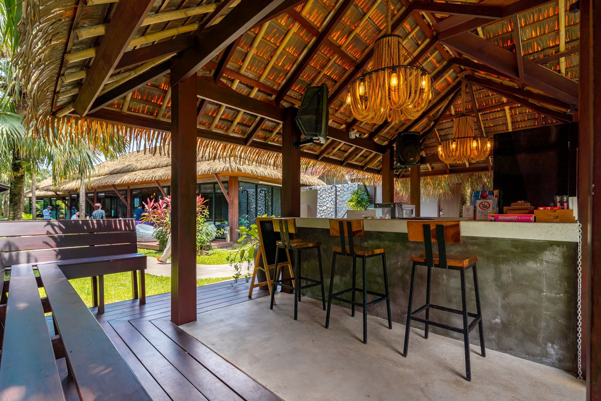 A wooden gazebo with a bar and chairs under a thatched roof.