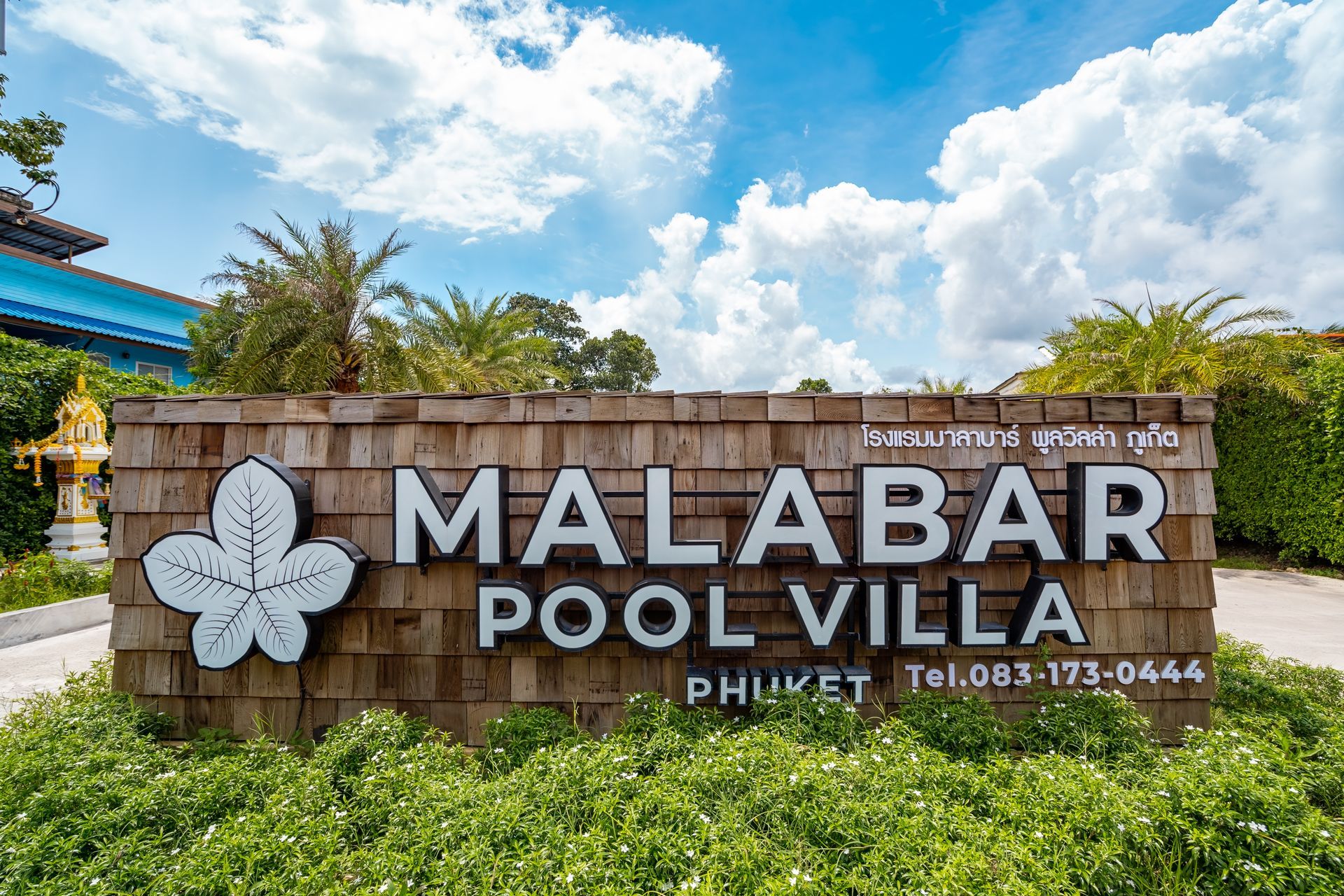 A wooden sign for malabar pool villa is surrounded by lush greenery.