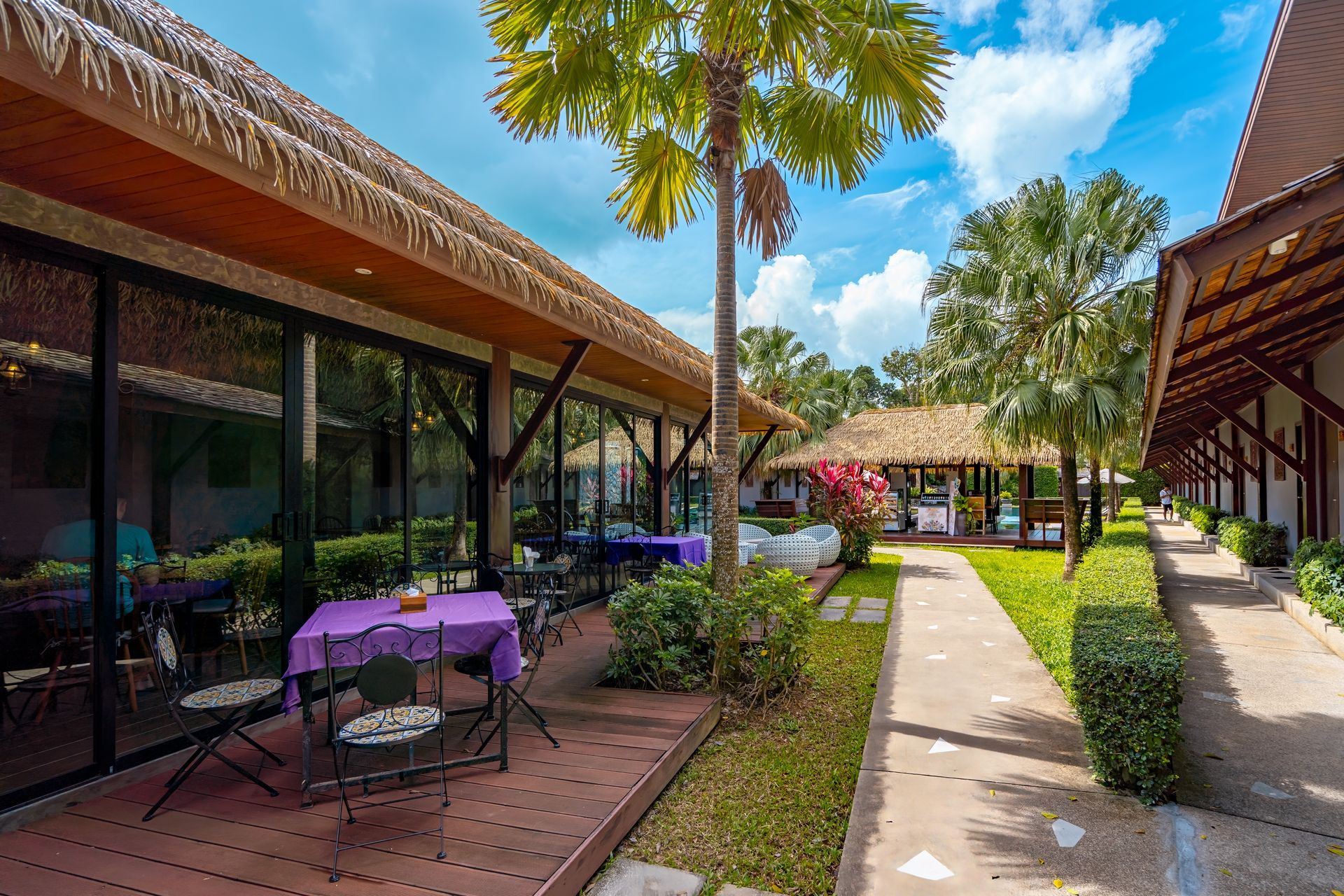 A patio with a table and chairs in front of a building with a thatched roof.