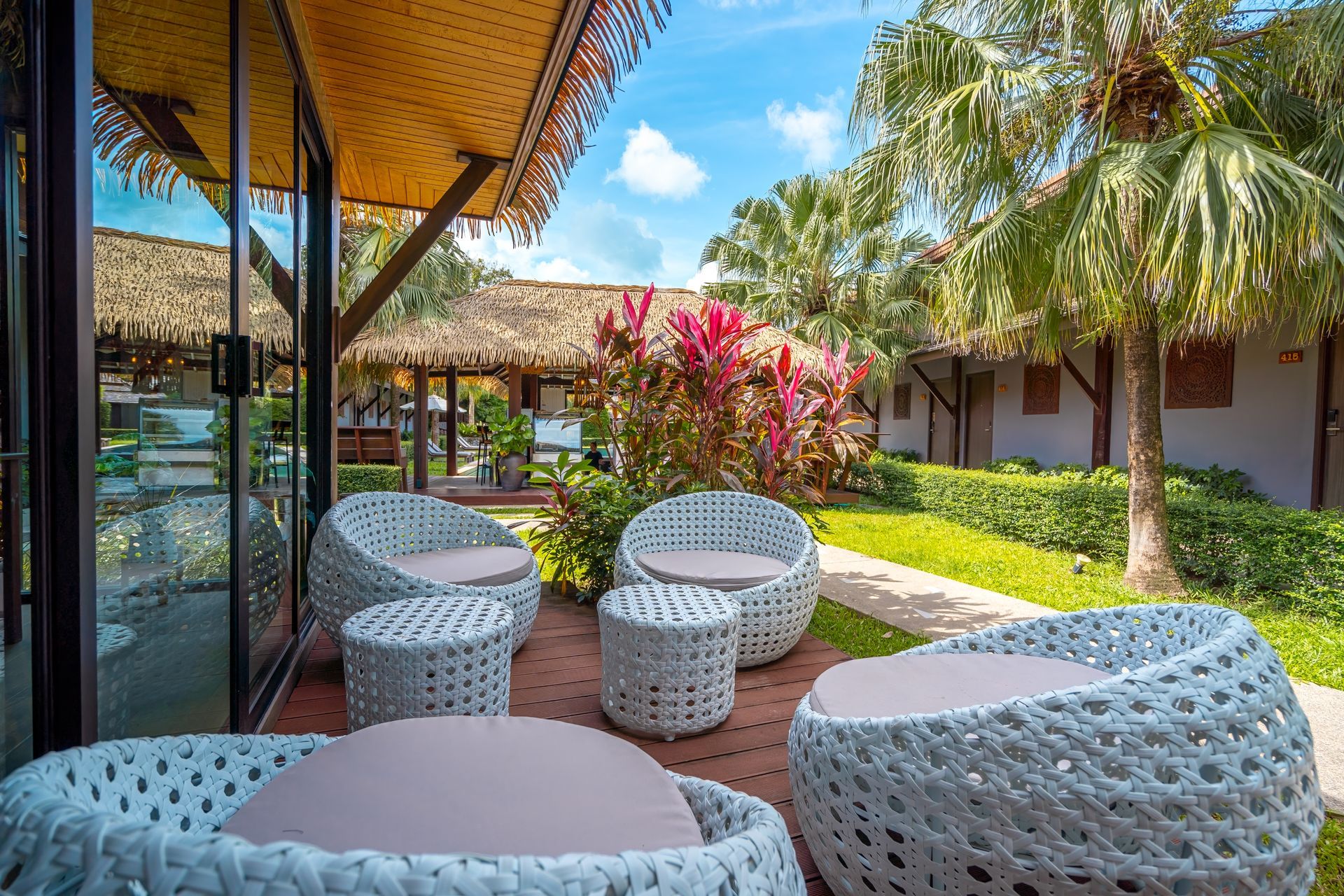 A patio with chairs , tables and a thatched roof.