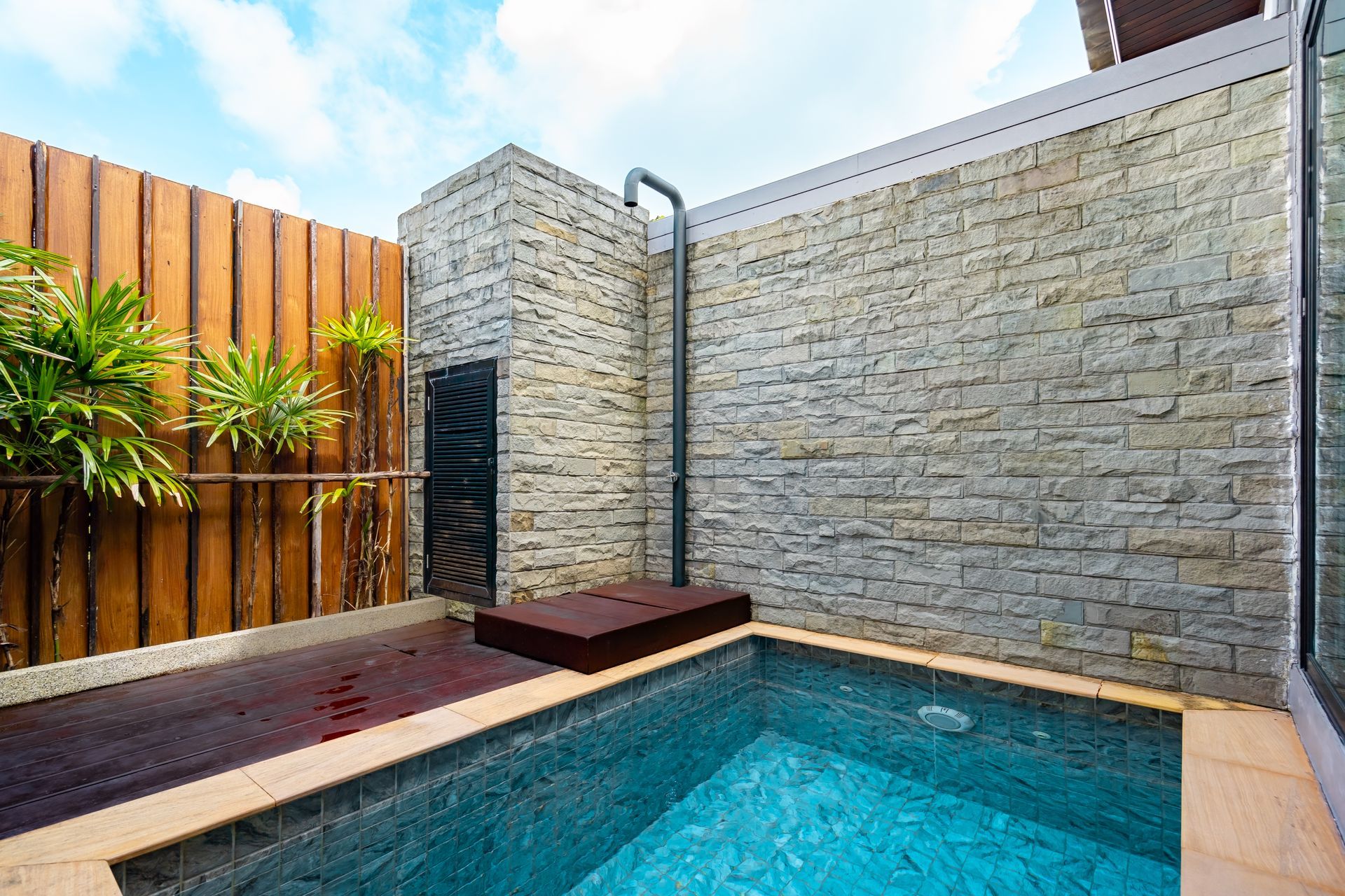 A small swimming pool surrounded by a brick wall and a wooden fence.