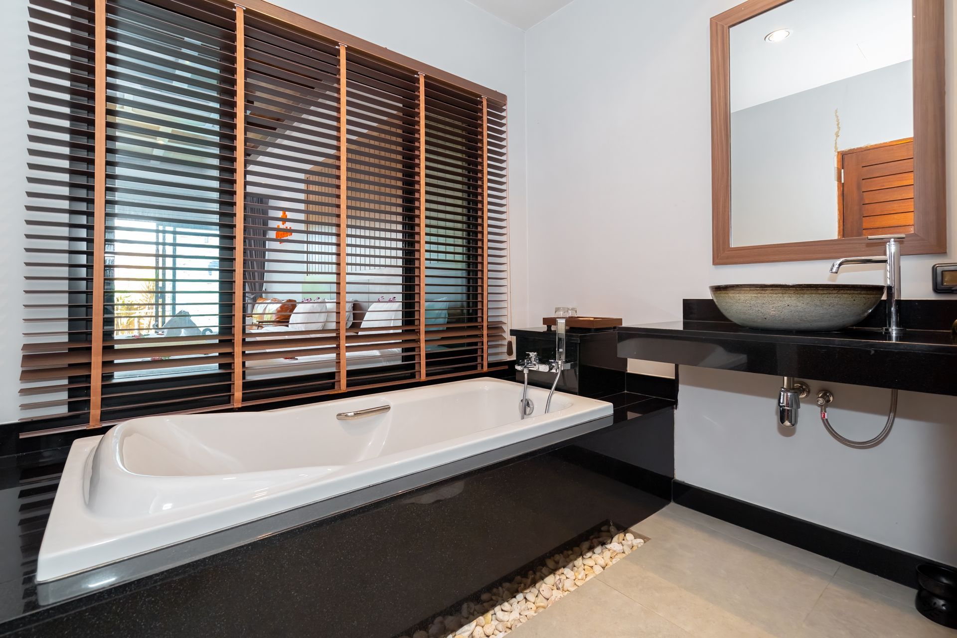 A bathroom with a bathtub , sink , mirror and blinds.