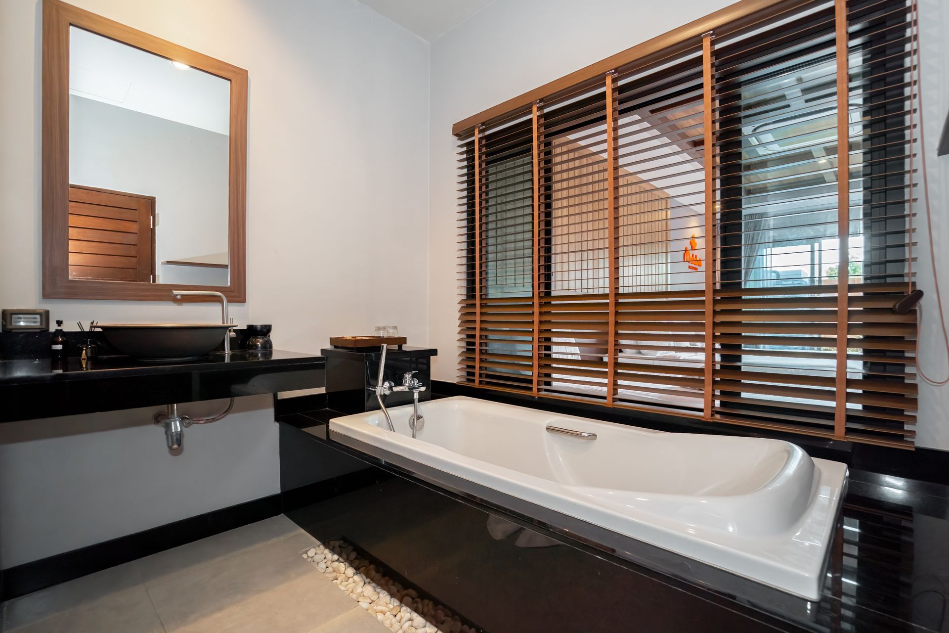 A bathroom with a bathtub , sink , mirror and blinds.