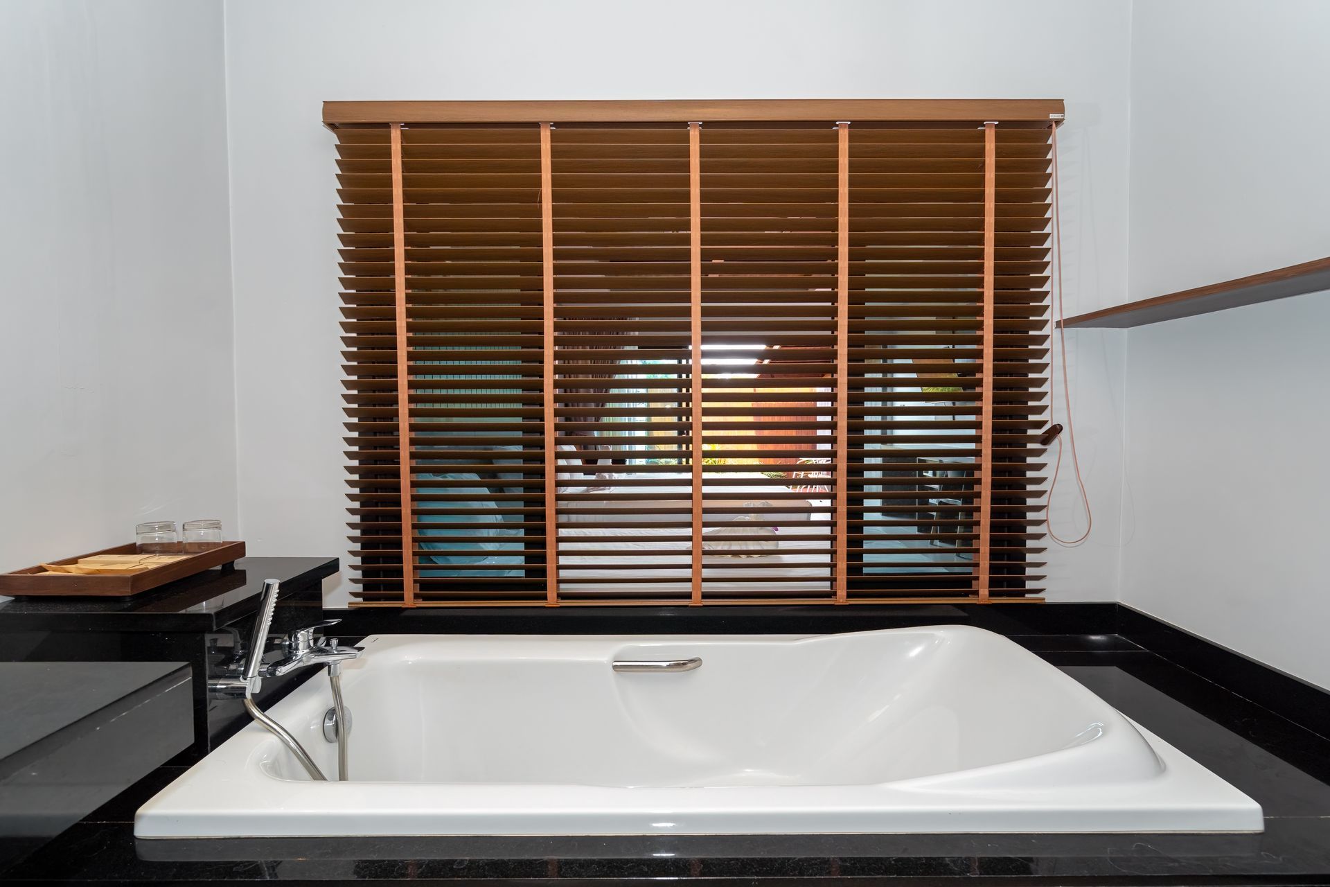 A bathroom with a bathtub and a window with blinds.