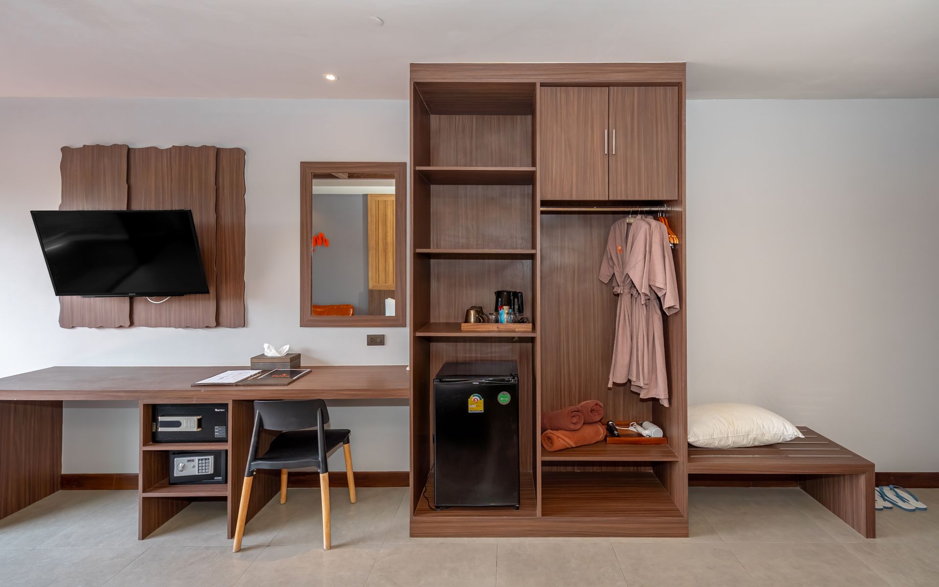 A hotel room with a desk , chair , television and a fridge.