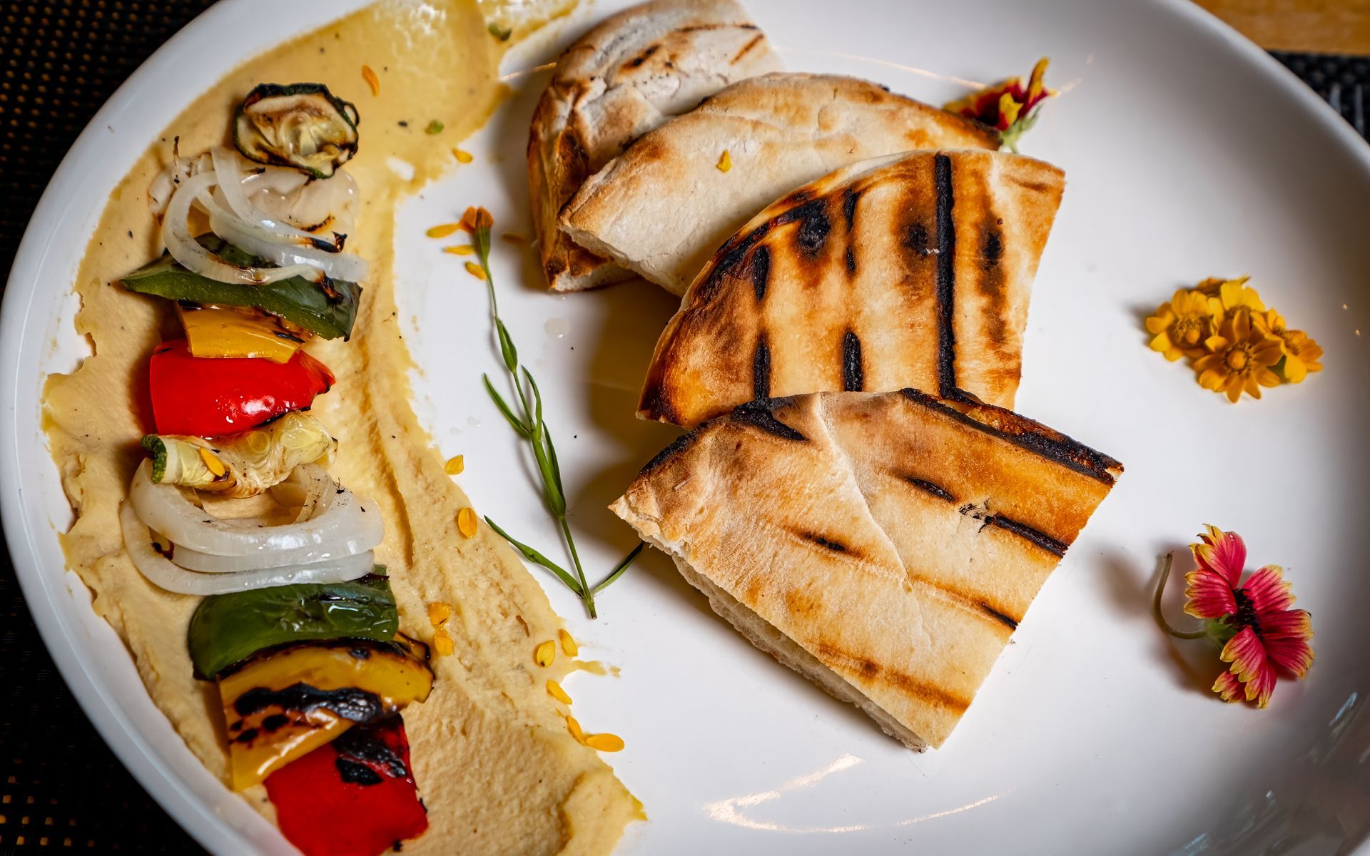 A white plate topped with pita bread , hummus and grilled vegetables.