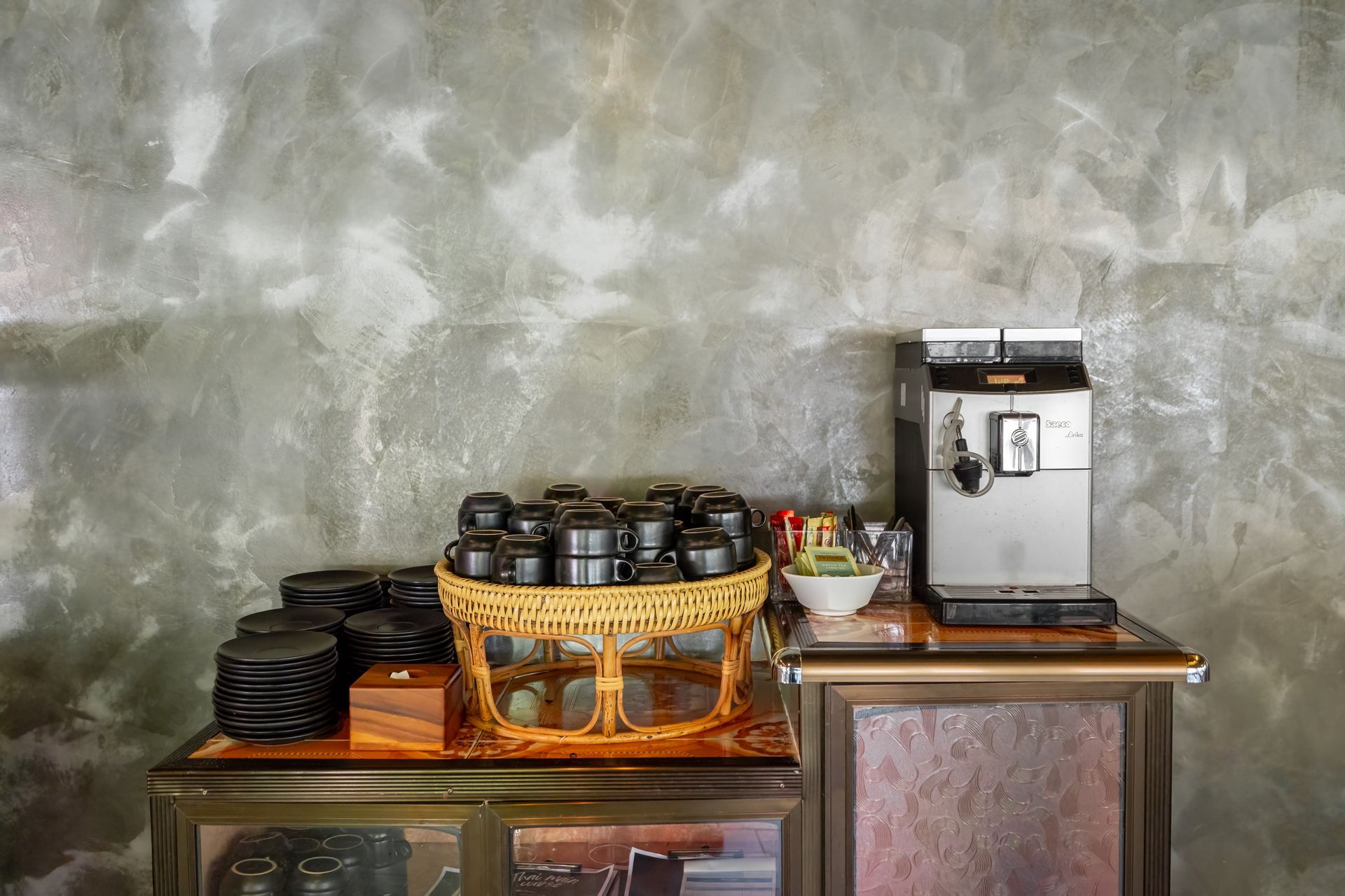 There is a coffee machine and a basket of cups on the table.