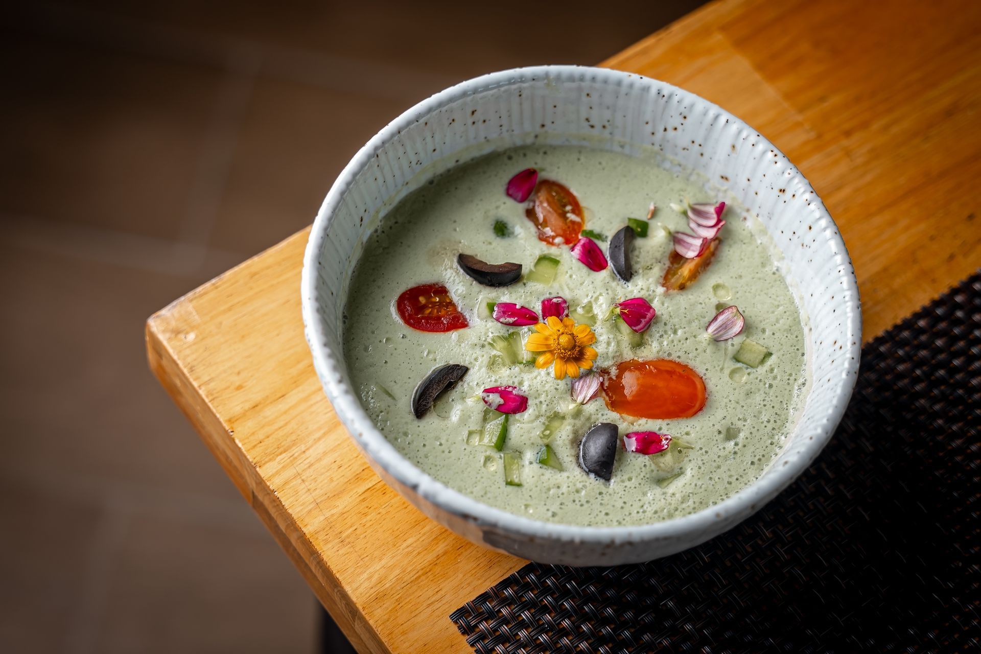 A bowl of soup with vegetables and flowers on a wooden table.