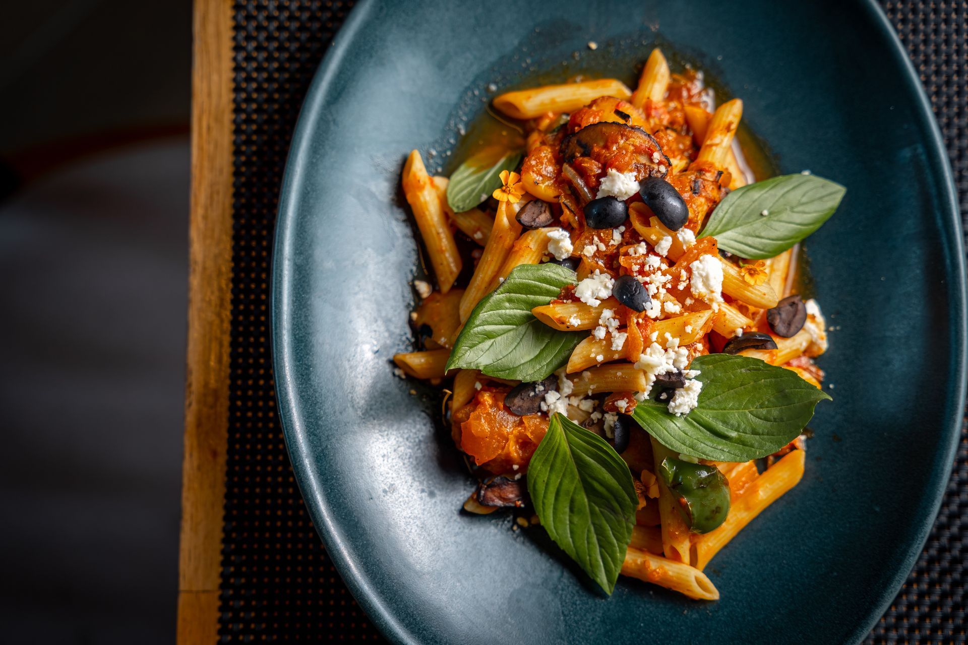 A blue plate topped with pasta and vegetables on a table.