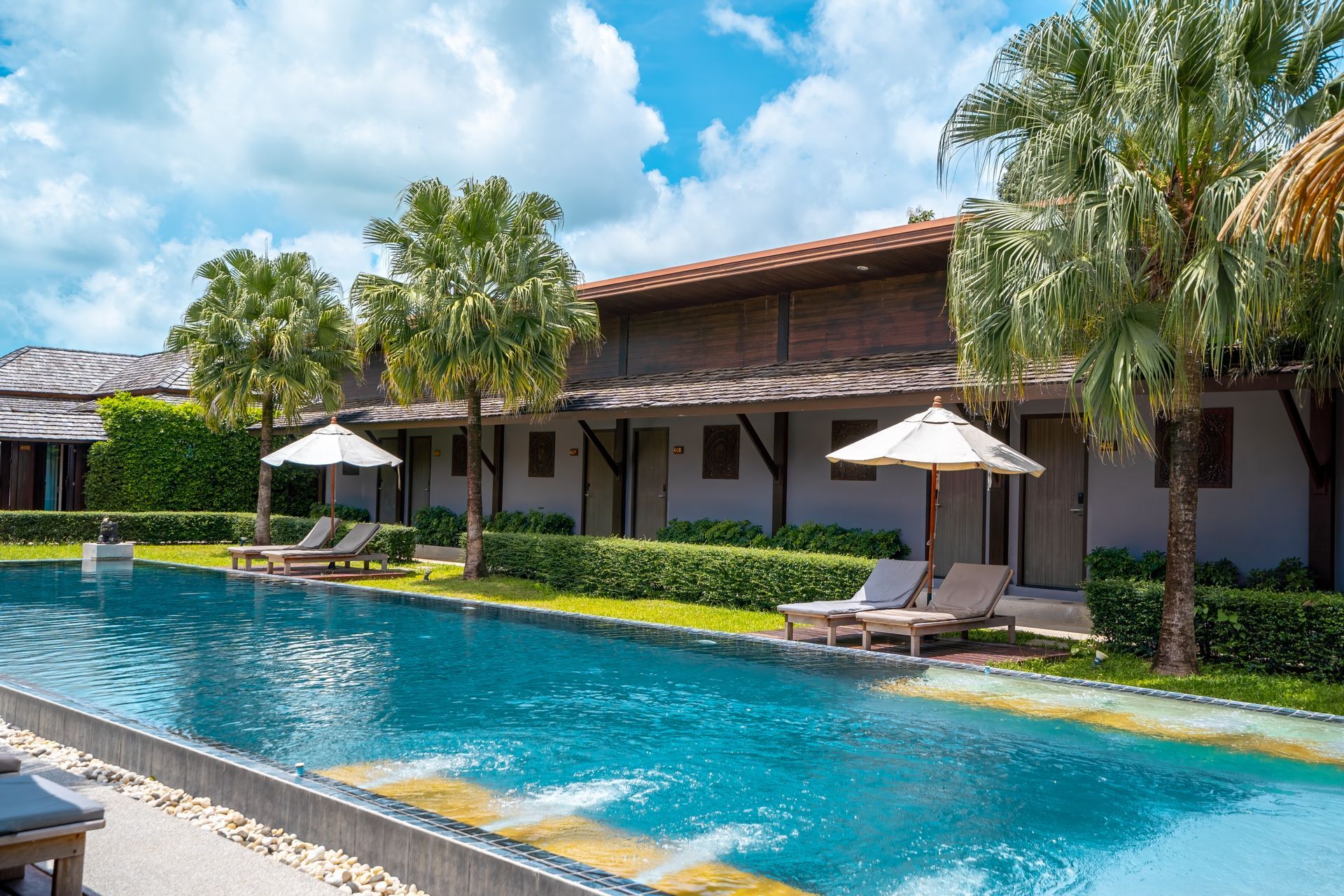 A large swimming pool surrounded by chairs and umbrellas in front of a hotel.