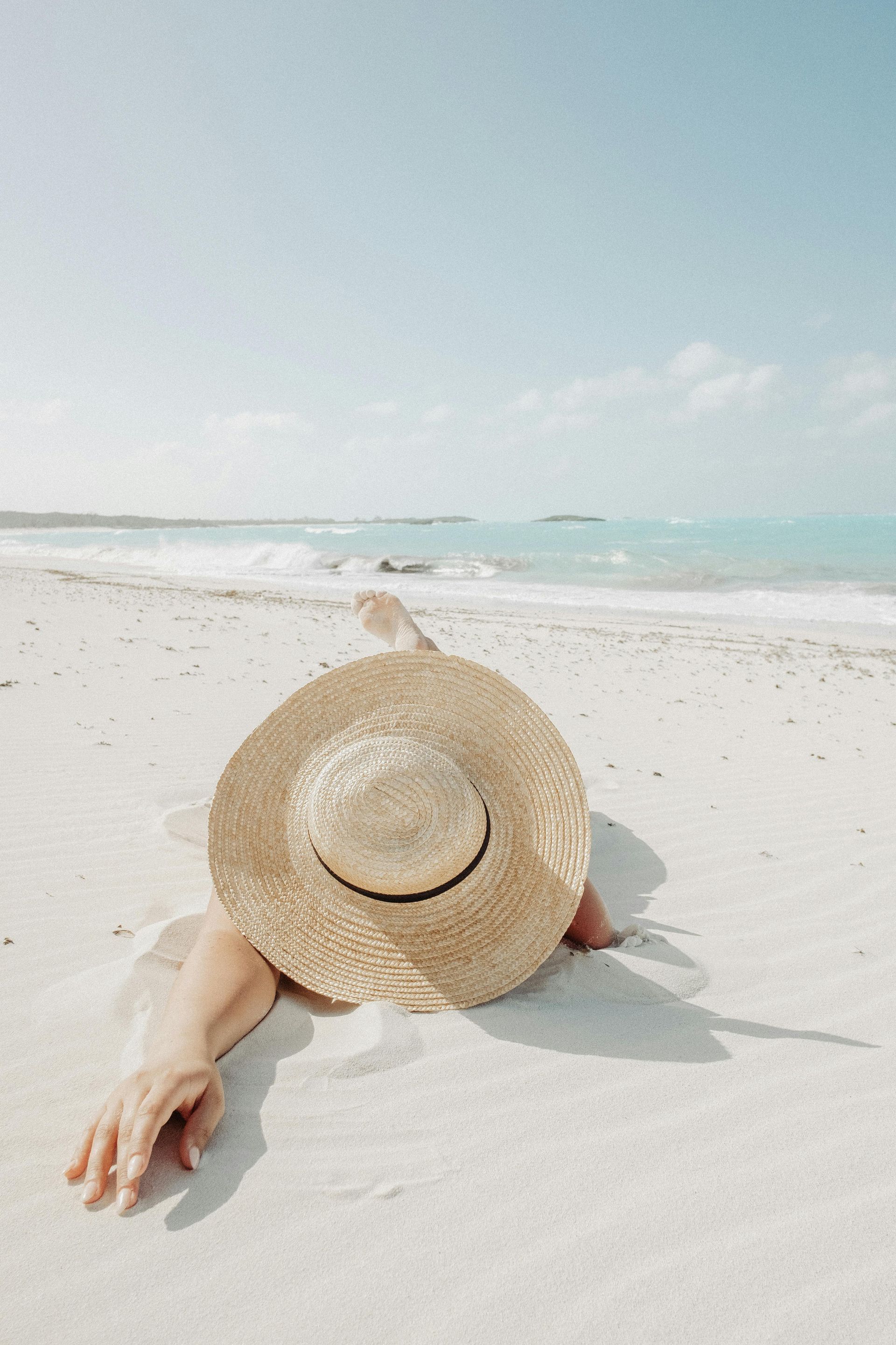 A woman is laying on the beach with a straw hat on her head.