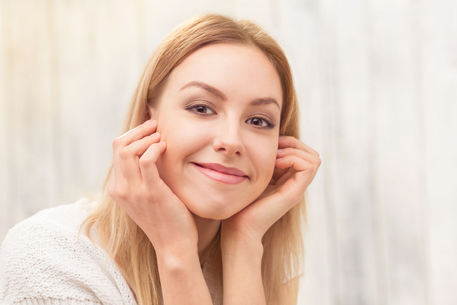 A woman is smiling and touching her face with her hands.