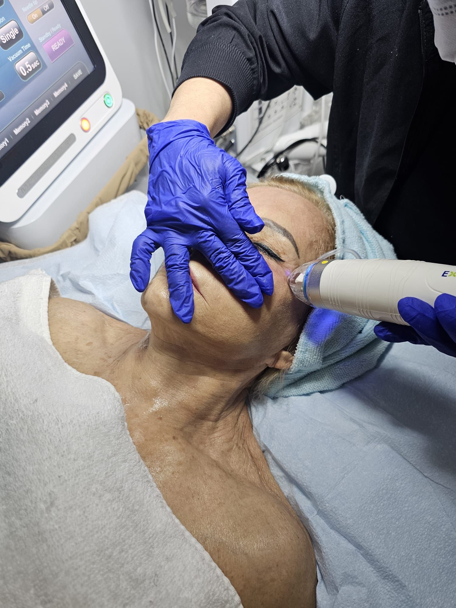 A woman is laying on a bed getting a treatment on her face.