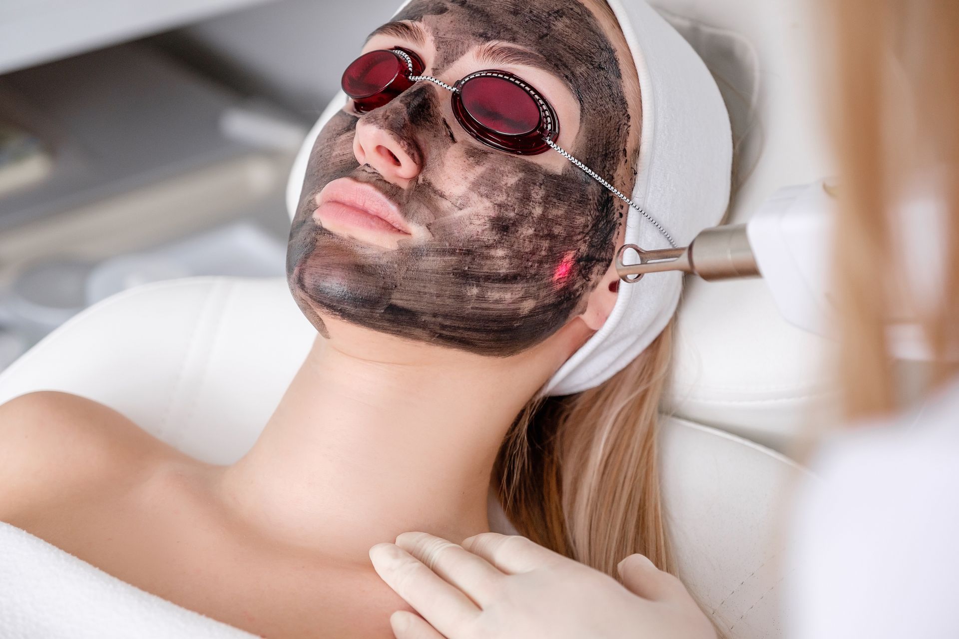 A woman is getting a charcoal mask on her face.