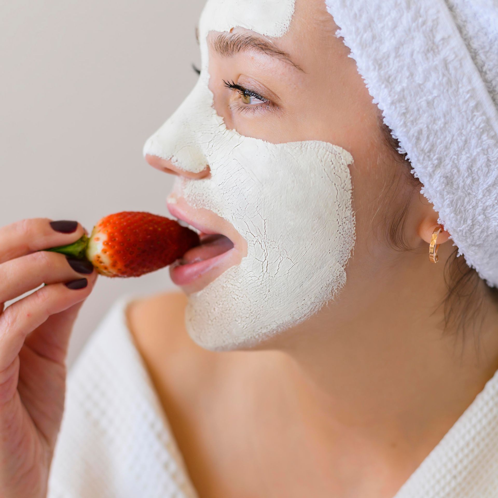 A woman with a white mask on her face is eating a strawberry.