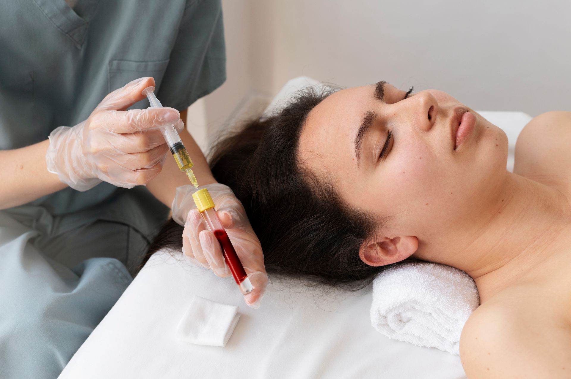 Person receiving a procedure. A technician is injecting a substance. Blood tube, syringe, white towel.
