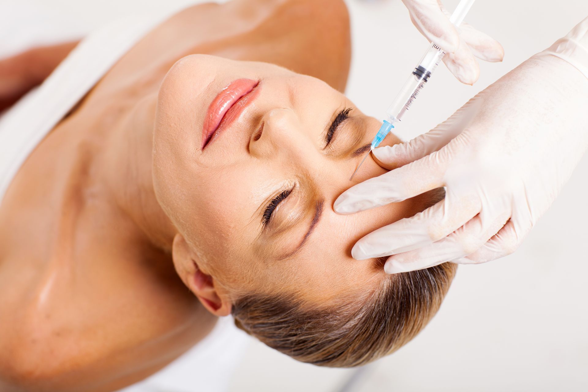 A woman is touching her face with her finger and smiling.