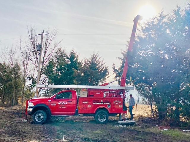 Red work truck with extended arm near trees; person working outdoors under a bright sun.