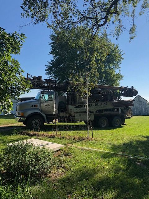 Well drilling truck parked on a grassy lawn with a tree and a blue sky in the background.