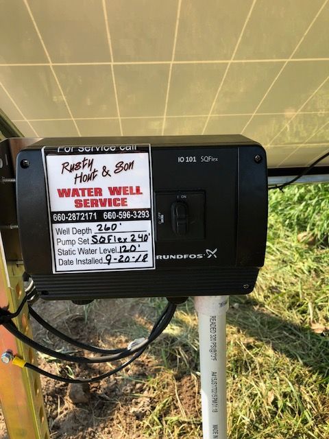 Black water well pump box with a service sticker, mounted near a solar panel.