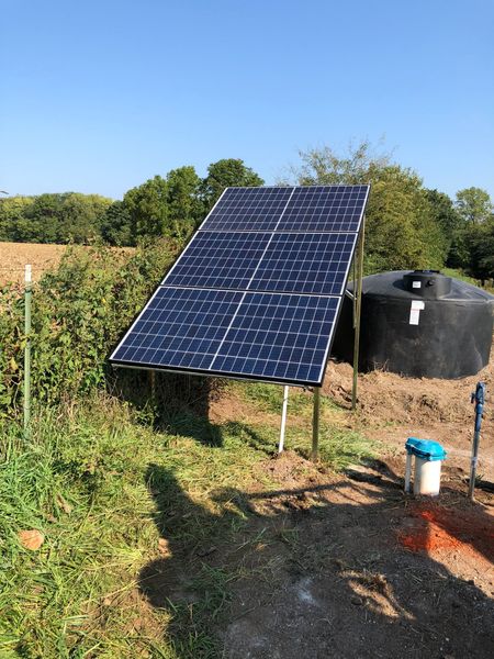 Solar panel powering water tank in a rural field, under a blue sky.