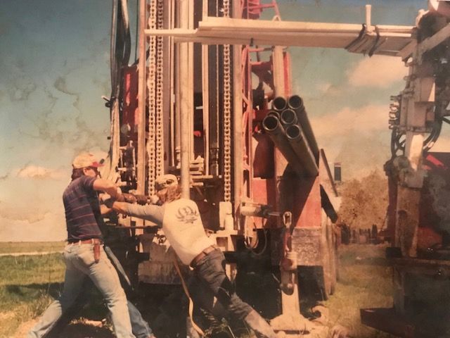 Men working with a drilling rig outdoors, likely installing well casing pipes.