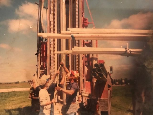 Drilling rig with two workers installing pipes in a field.