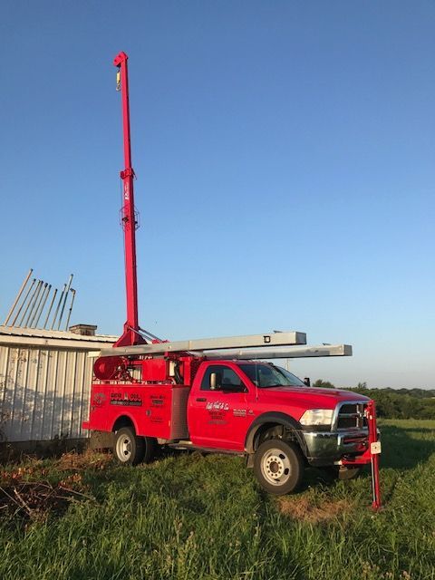 Red utility truck with a crane parked near a building in a field on a sunny day.