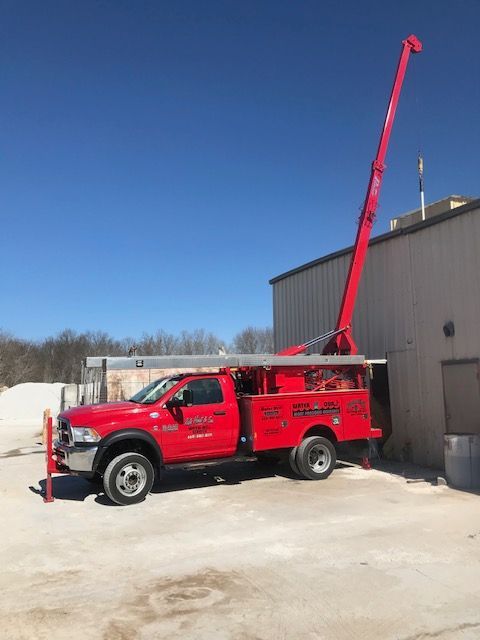 Red service truck with extended boom, parked next to a building on a sunny day.