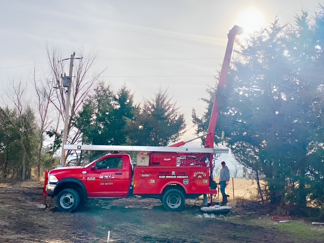 Red utility truck with extended boom, man working; sunny outdoor setting.