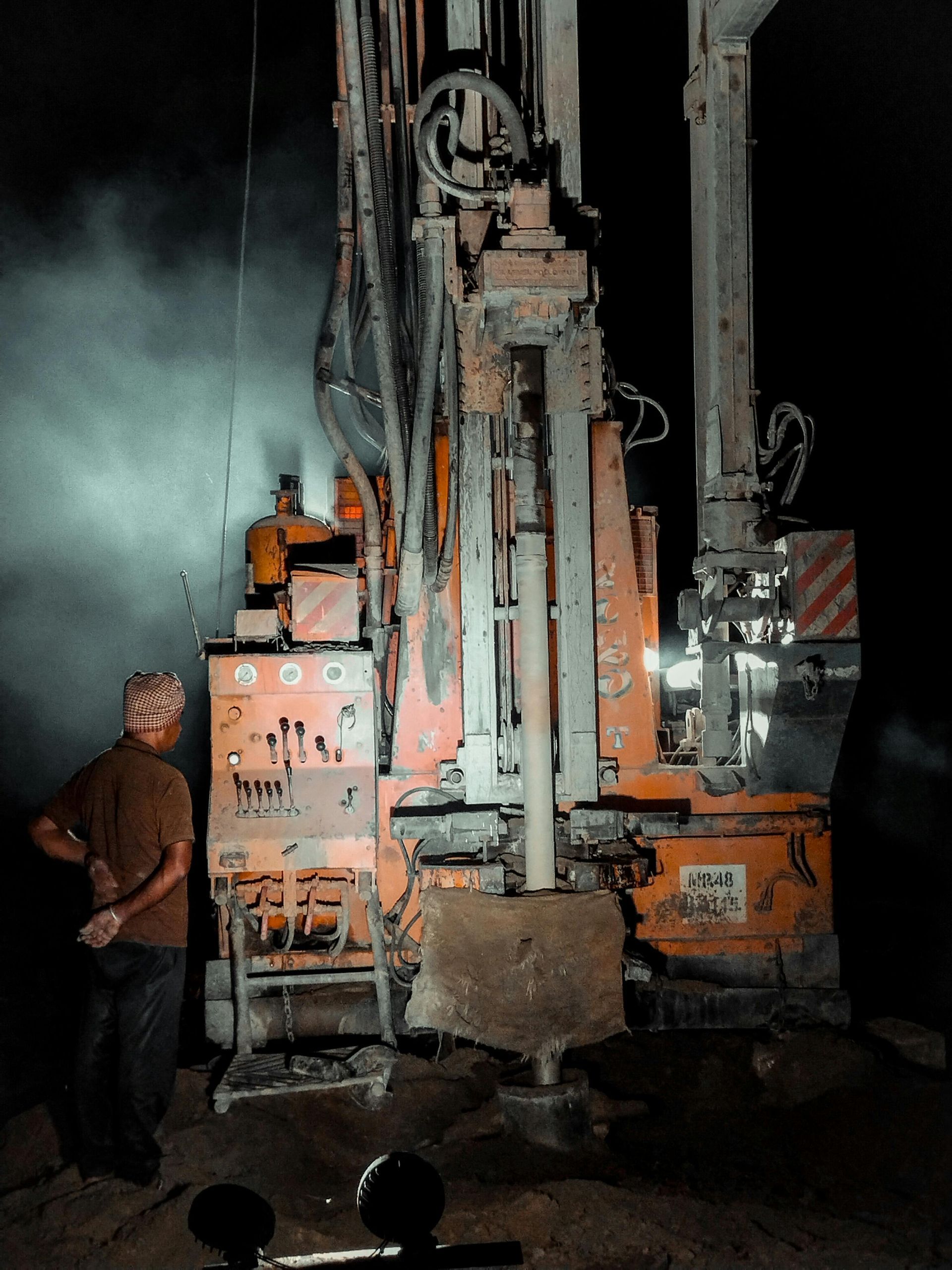 An orange drilling rig operating at night, a person stands nearby.