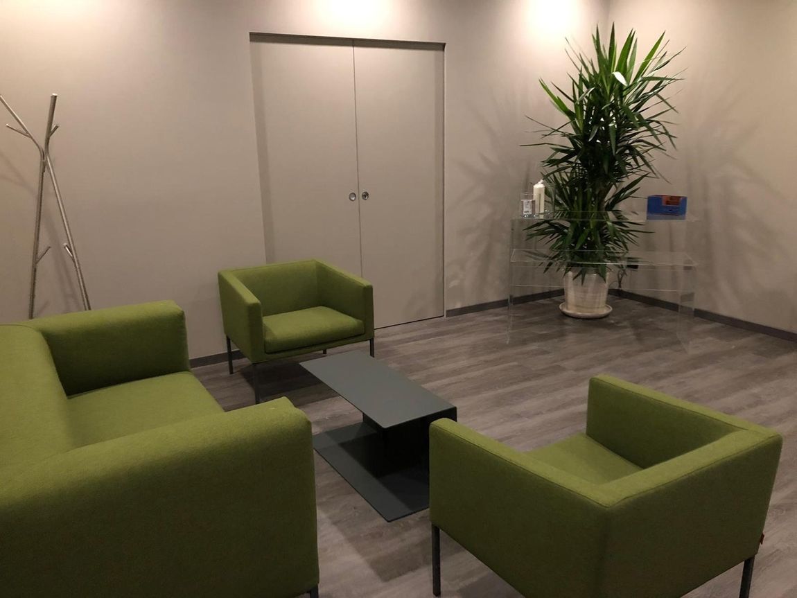 Salotto moderno con poltrone verdi, tavolino basso nero, pianta in vaso e doppie porte chiuse.