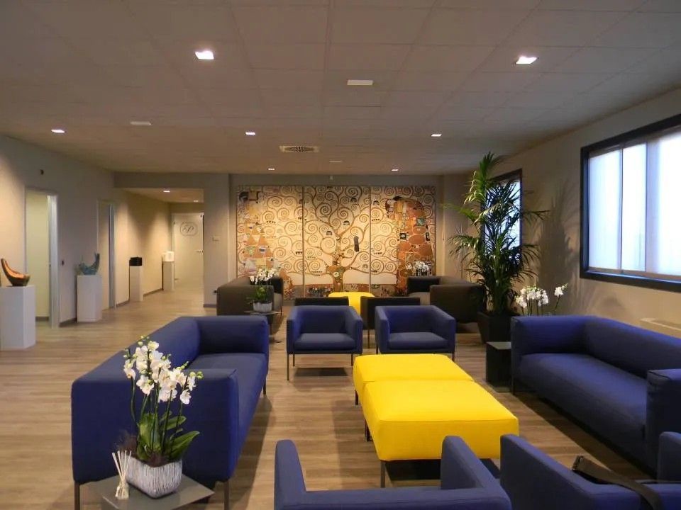 Sala d'attesa moderna con divani blu, tavolini giallo brillante e un grande murale in una zona ben illuminata.