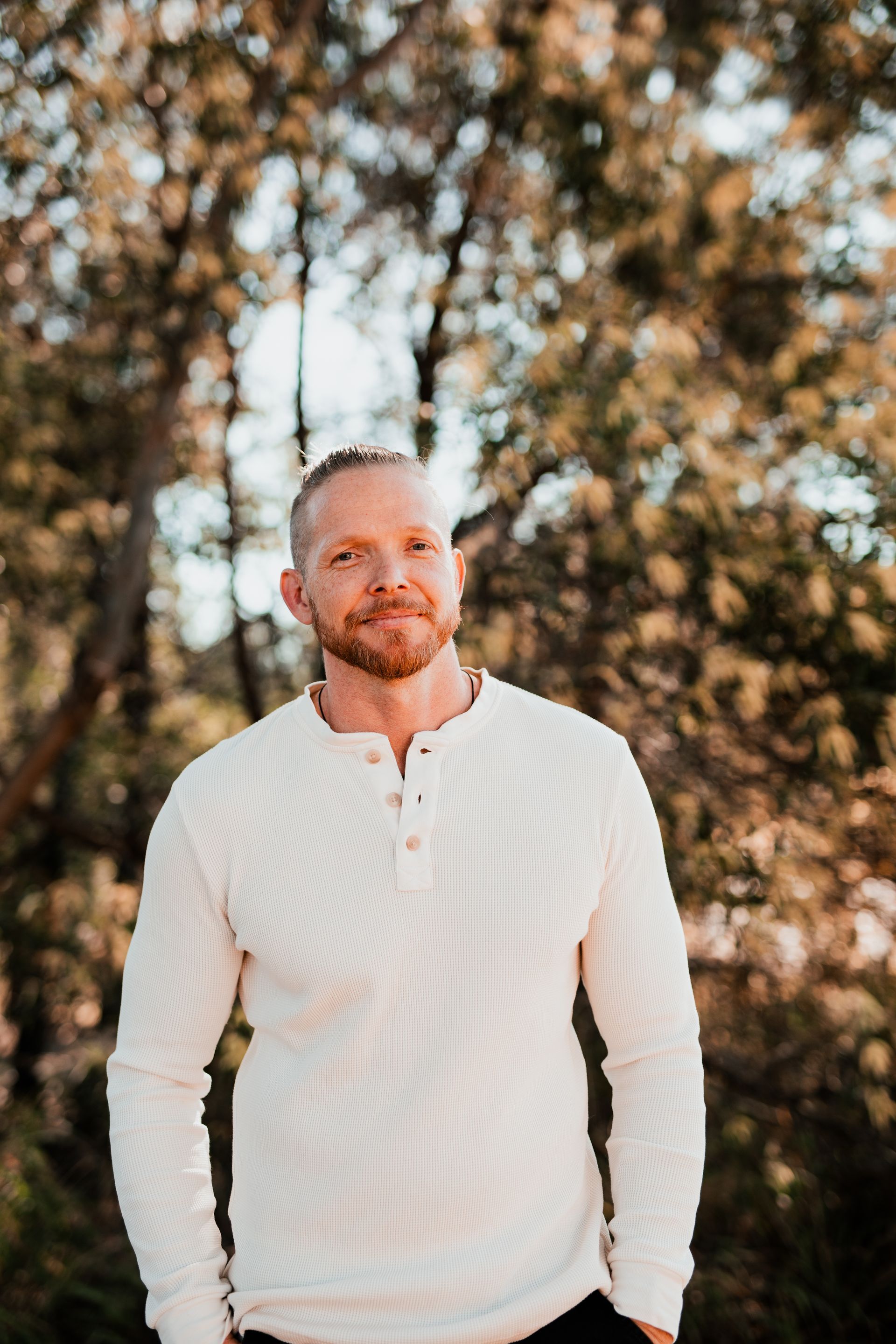 Trent in a pink shirt and blue pants is standing in front of a wooden wall.