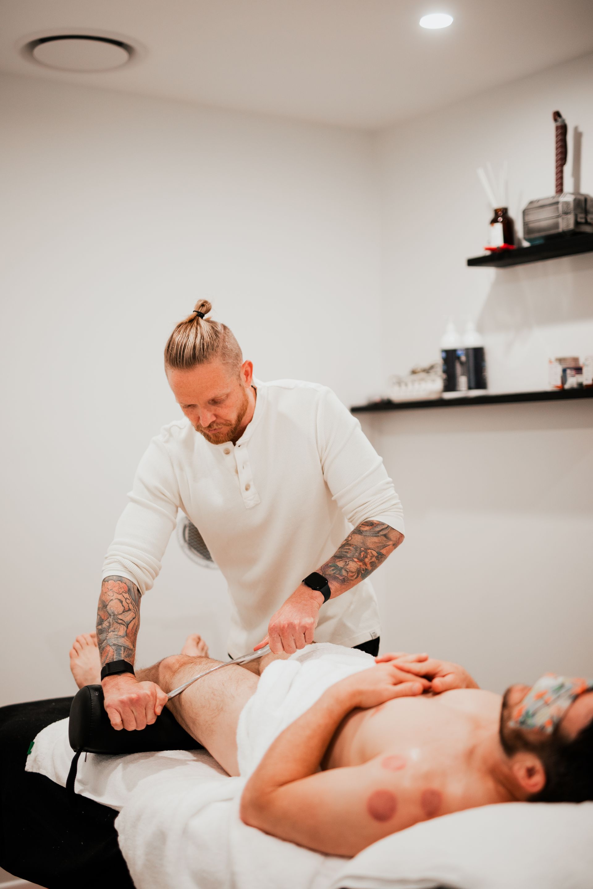 A man is laying on a bed getting a IASTM from a massage therapist.