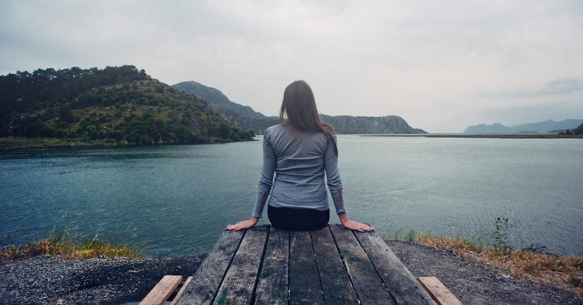 A woman is sitting on a wooden dock overlooking a lake.