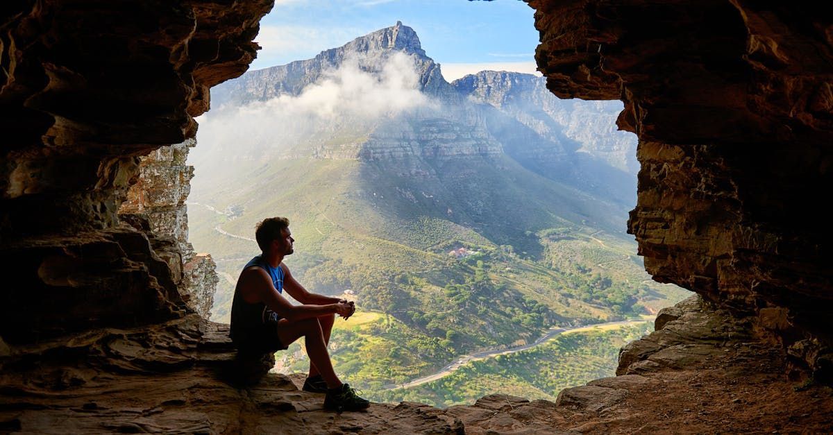 A man is sitting in a cave looking out at a mountain.