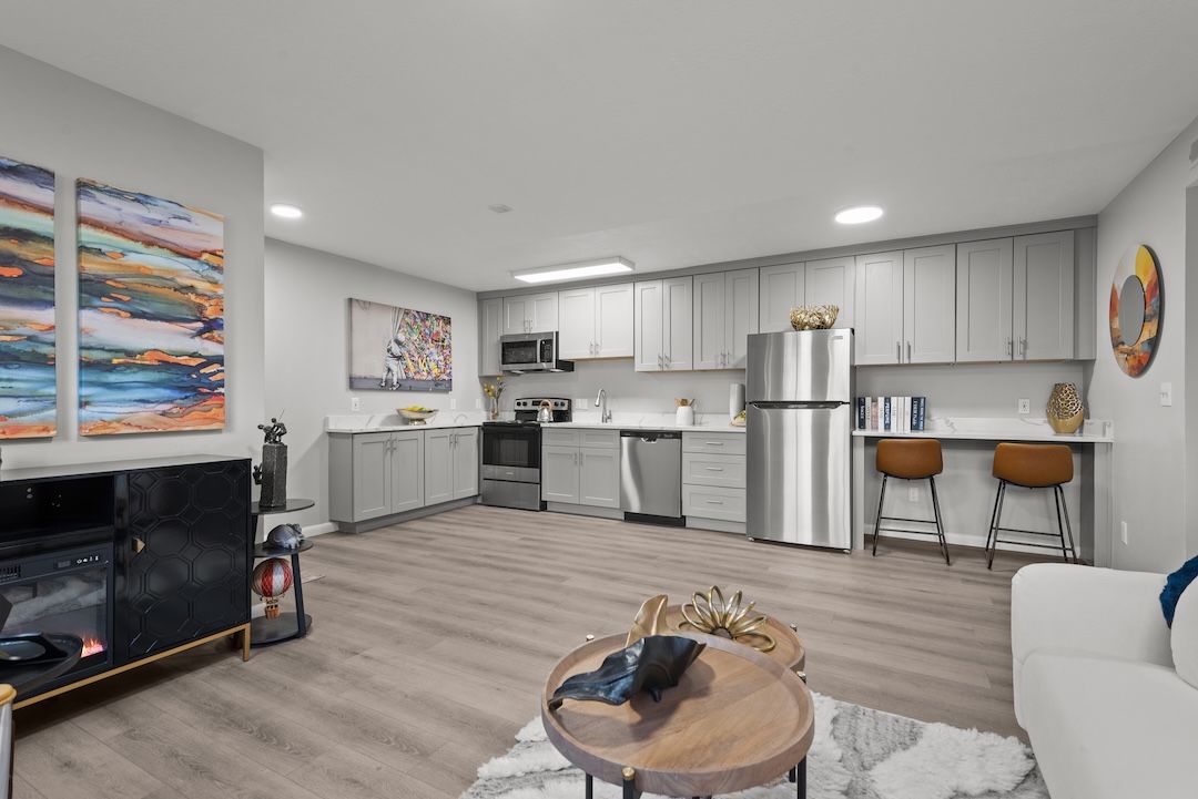 Modern open-plan living room with kitchen, gray cabinets, wood floor, couch, TV, and dining nook