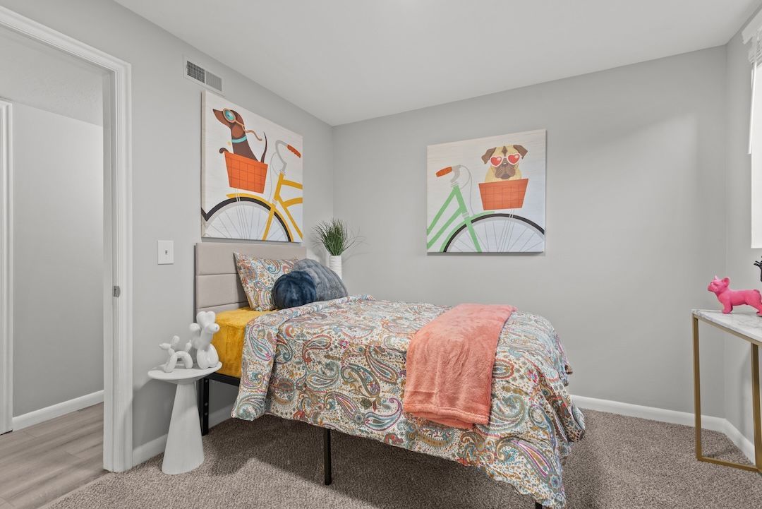 Small bedroom with a twin bed, floral bedding, orange accent pillow, and colorful wall art.