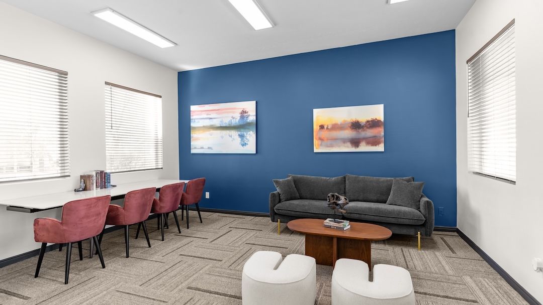 Modern waiting room with blue accent wall, gray sofa, pink chairs, and coffee table near windows