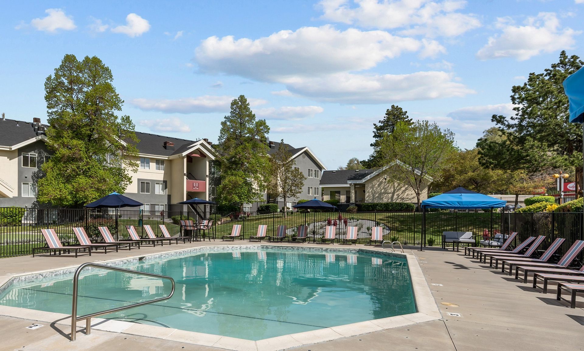 A large swimming pool surrounded by chairs and umbrellas in front of a building.
