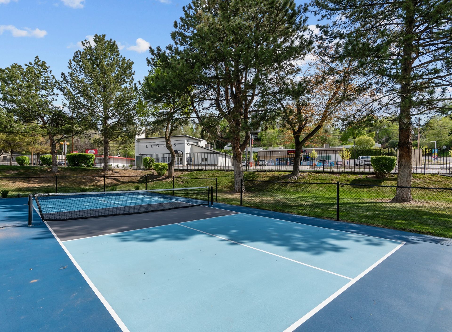A tennis court in a park with trees in the background.