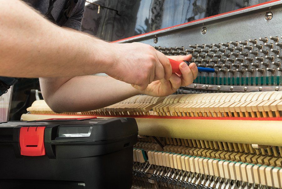 Person repairing a piano with tools, focusing on the internal mechanisms of the instrument.