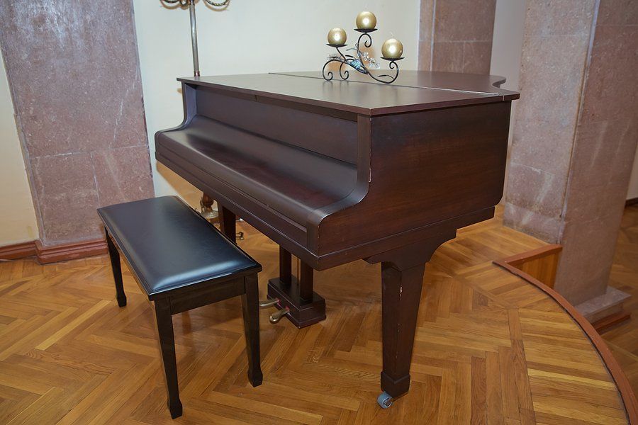 A grand piano with a black bench, positioned in a room with hardwood floors.