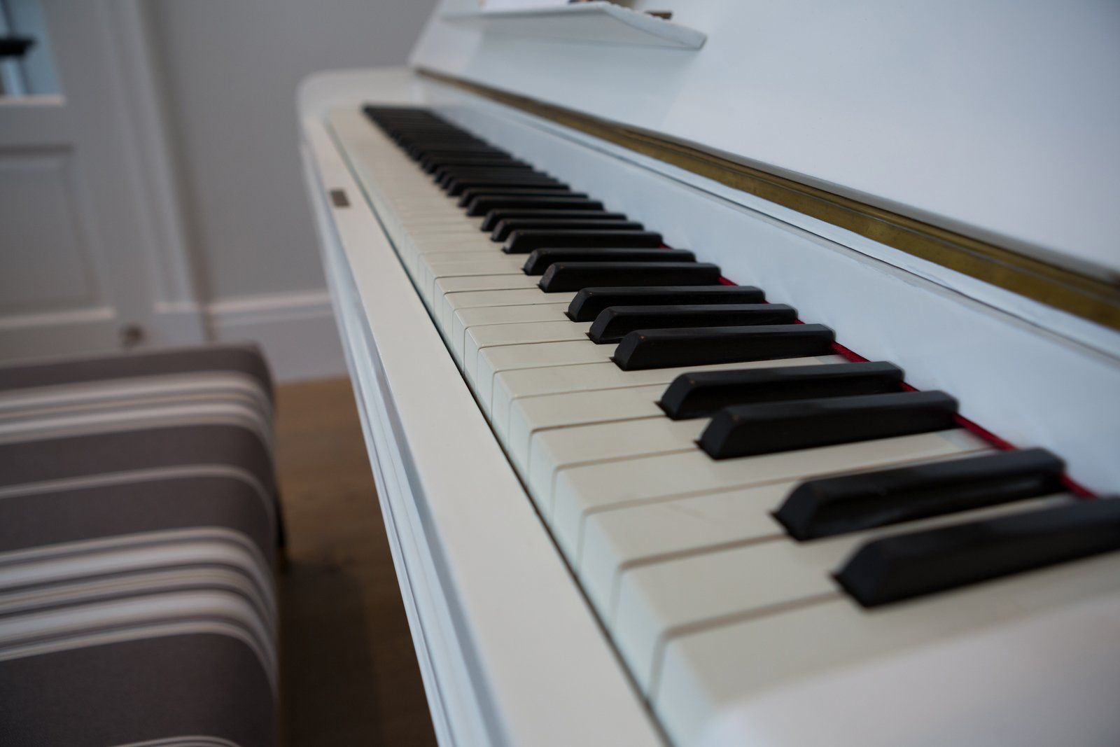 White piano keyboard with black and white keys, a striped stool in the foreground.