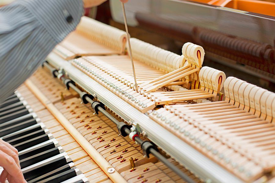 Piano technician working on the internal mechanisms of a grand piano.