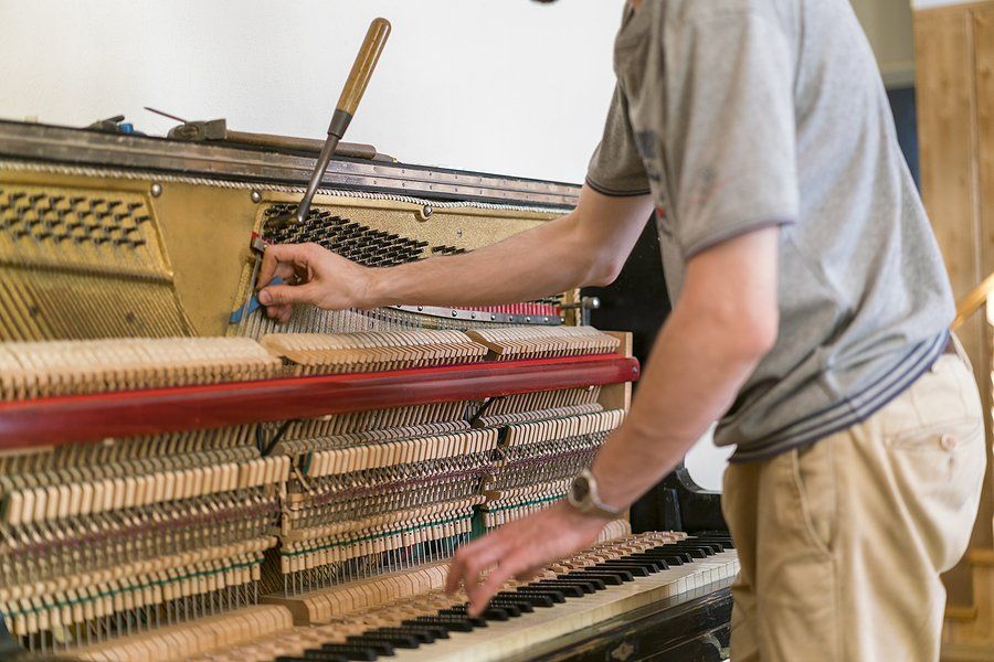 Person tuning a piano with a tool, focusing on the strings. Bright setting, with piano keys in view.