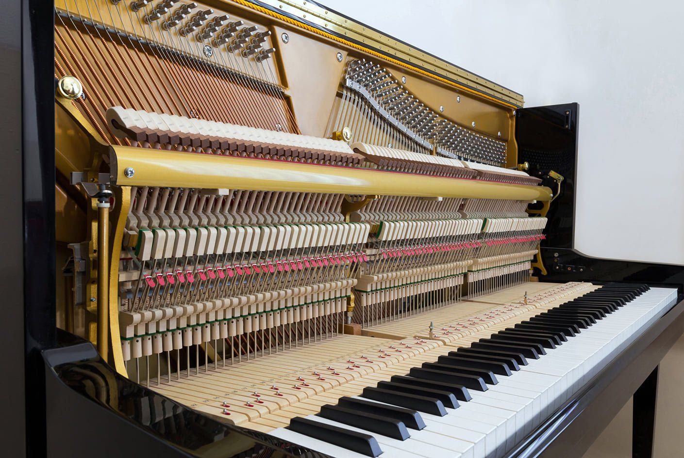 Open upright piano showing keys, hammers, and strings. Black exterior with gold-toned inner workings.