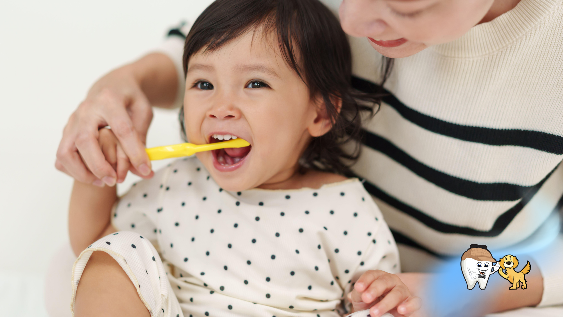A person brushes a child's teeth with a yellow toothbrush; both look happy.