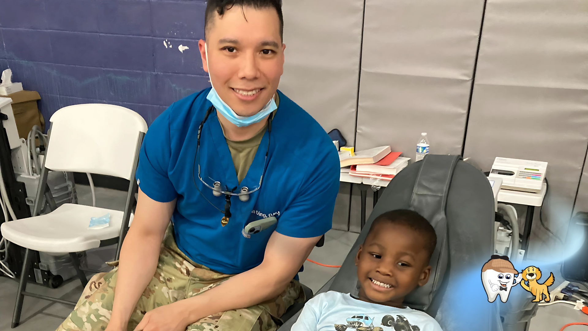 A dentist is sitting next to a young boy in a chair.